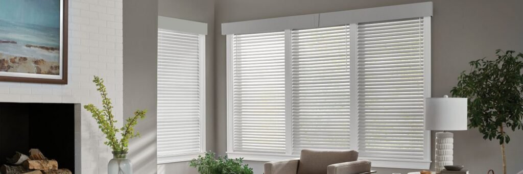 Living room with large windows fitted with white wood blinds and a narrow side window with matching blinds.