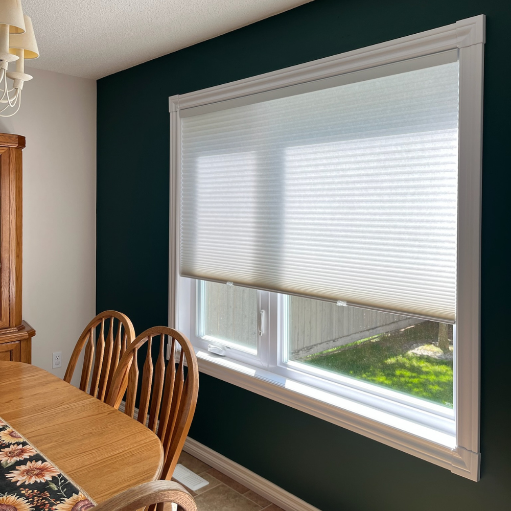 Energy-efficient honeycomb cellular shades for a dining room. This custom window treatment provides excellent insulation and light control, featuring a cordless design that pops against a modern dark green accent wall.