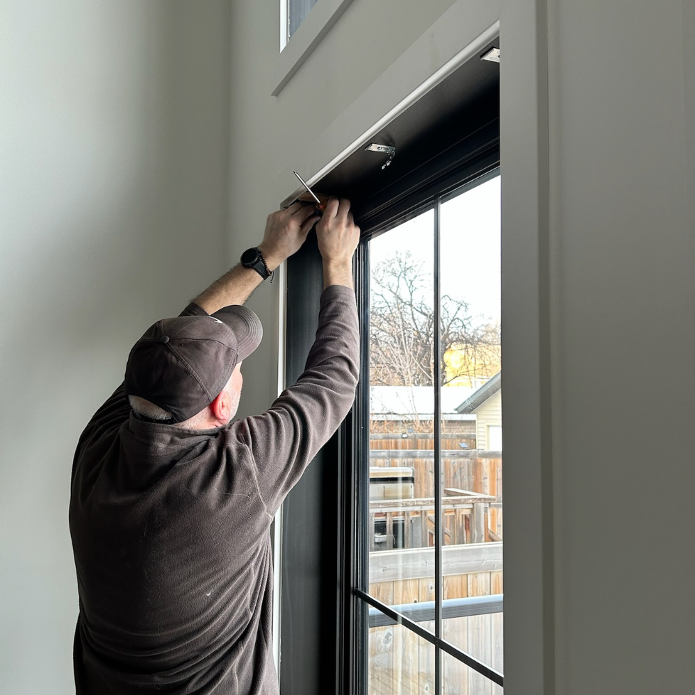 Expert installation of custom window blinds. A technician carefully mounts the headrail hardware for new shades, ensuring a secure and level fit for high-performance window coverings.