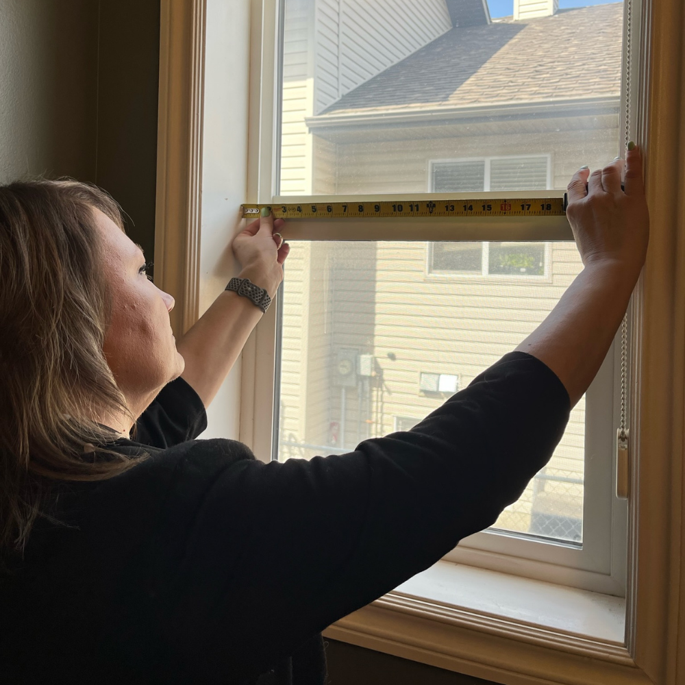 Professional window measurement for custom blinds. A consultant measures the horizontal width of a window frame to ensure a perfect fit for new Alta window coverings.