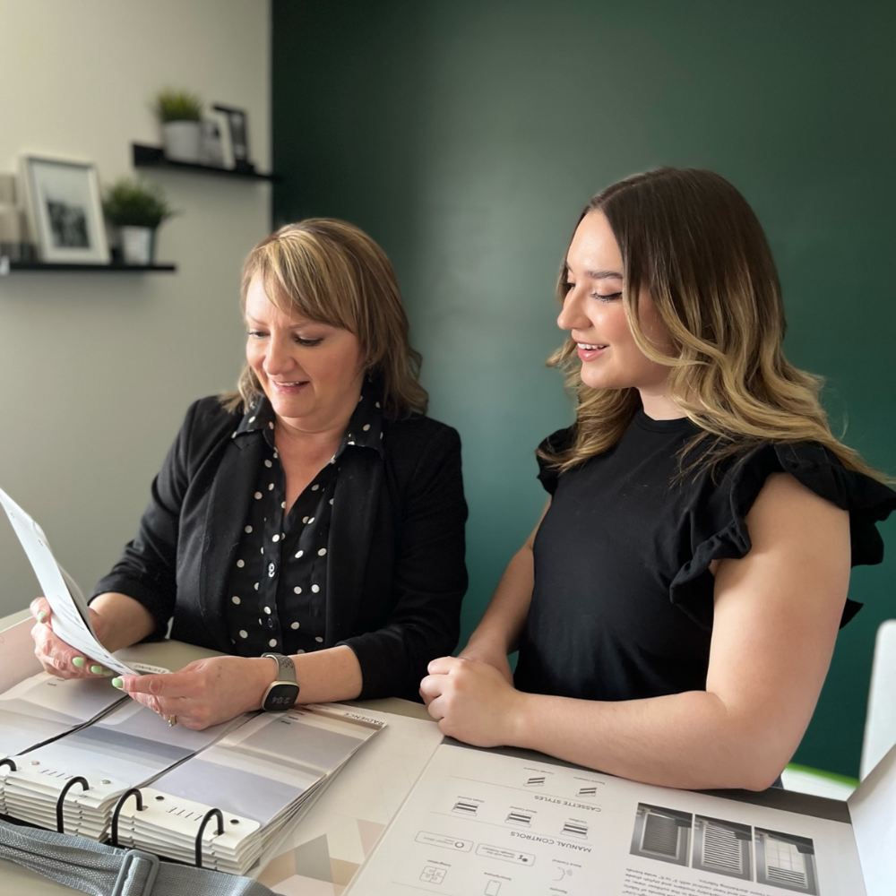 Finalizing a custom blinds quote during an in-home consultation. A design expert presents pricing and product options from an Elite window fashions catalog to a happy customer, ensuring transparency and professional service.
