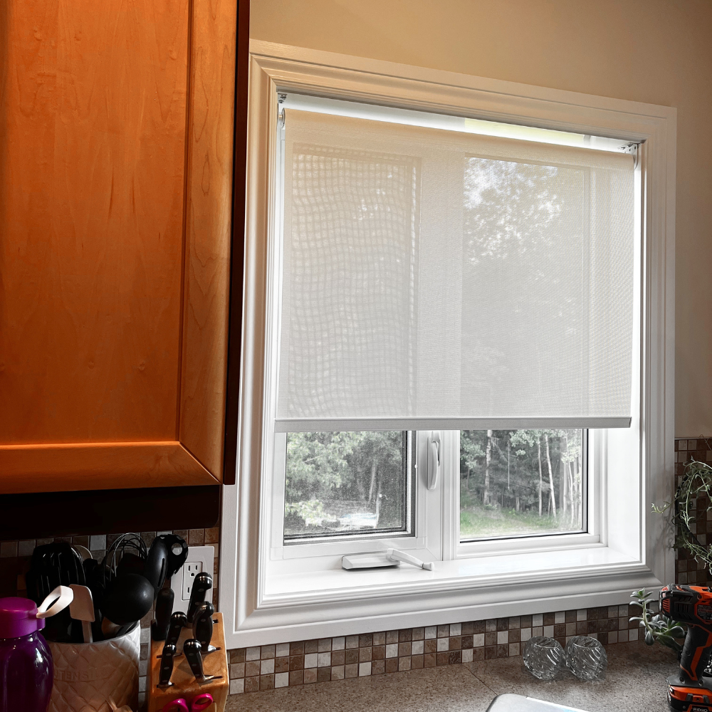 Custom light-filtering roller shades for a kitchen. This professional installation features a clean, cordless design that provides privacy and UV protection while complementing modern kitchen decor and wood cabinets.